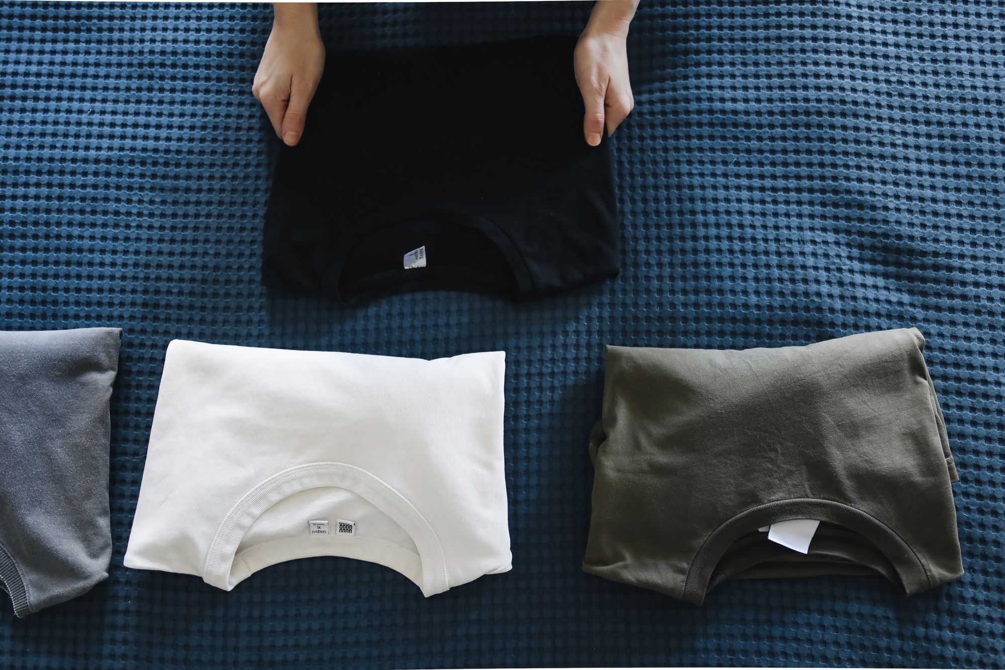 Folded t-shirts laid out on a blue blanket.