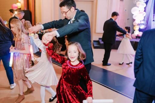 A father and daughter dancing together at a party decorated with balloons and warm lights.