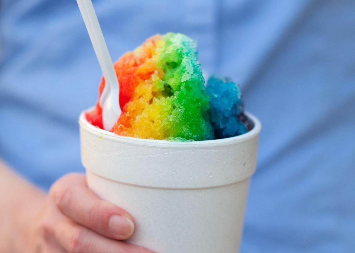 A cup of rainbow shaved ice with a white spoon.