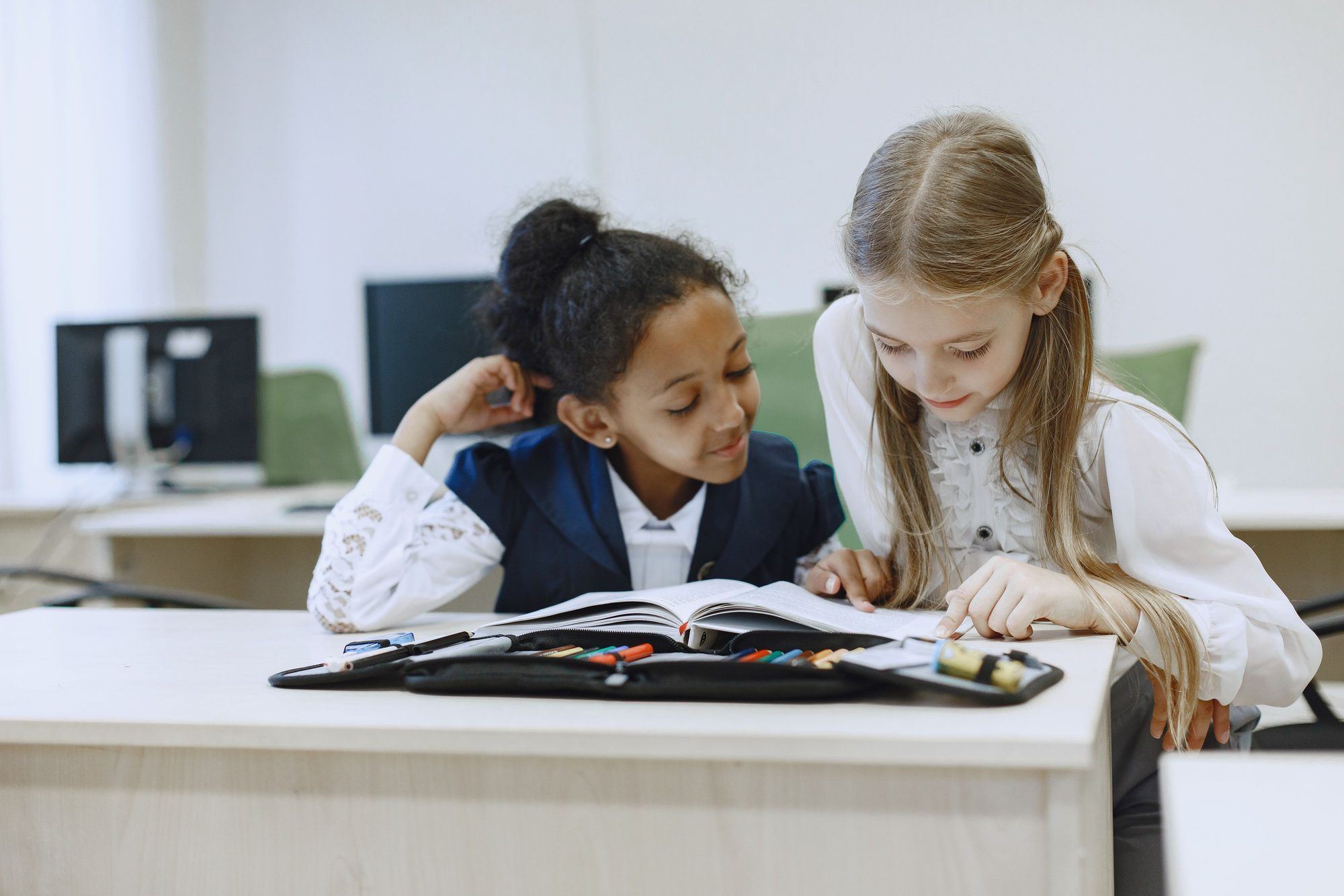 Two students looking through an open book together at a classroom table.